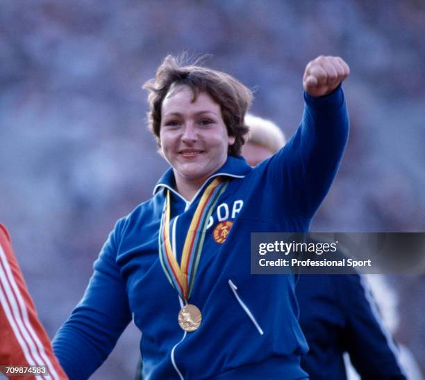 East German discus thrower Evelin Jahl raises one arm in the air in celebration on the medal podium after finishing in first place to win the gold...