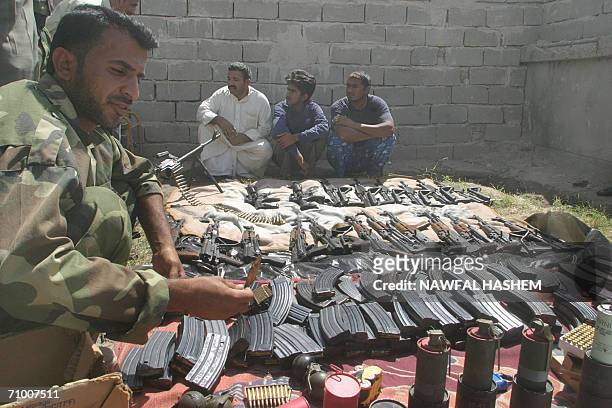 An Iraqi police commando displays confiscated arms as three alledged Pakistani infiltrators sit in the custody after they were arrested in Safwan on...