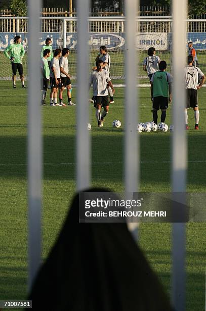 An Iranian woman watches a training session of Iran's national football team from behind a fence as females were not allowed to enter the stadium at...