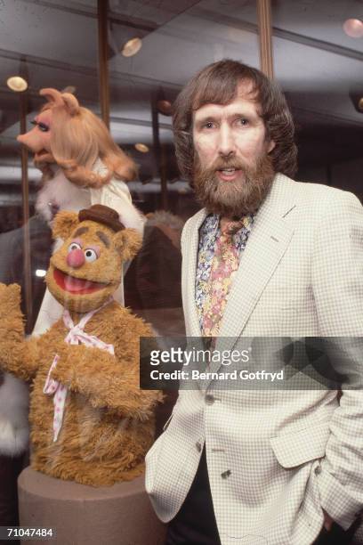 American film & televison director and puppeteer Jim Henson stands with his hands in his pants pockets and poses with his muppets Fozzie Bear and...