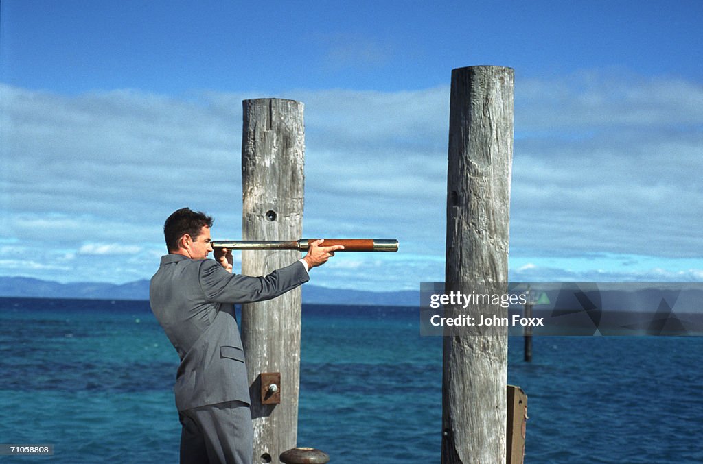 Businessman looking at sea through telescope, side view