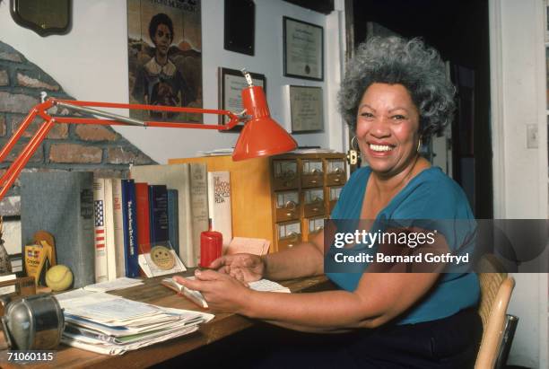 Portrait of American author Toni Morrison smiling and sitting at her desk at home, 1980s.