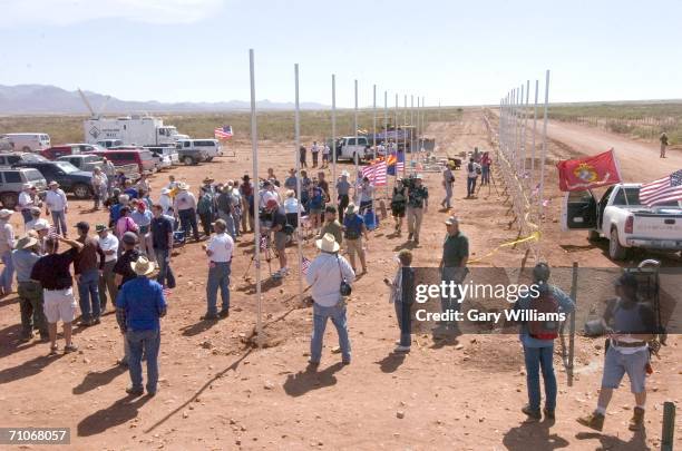Volunteers of the Minuteman Civil Defense Corp. Put up barb wire along new fencing topped by American flags on a line of new fence posts on May 27,...