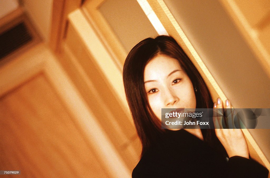 Young woman standing by doorway, smiling, portrait 