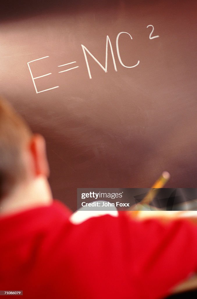 Boy at desk in front of blackboard, 'E=MC2'