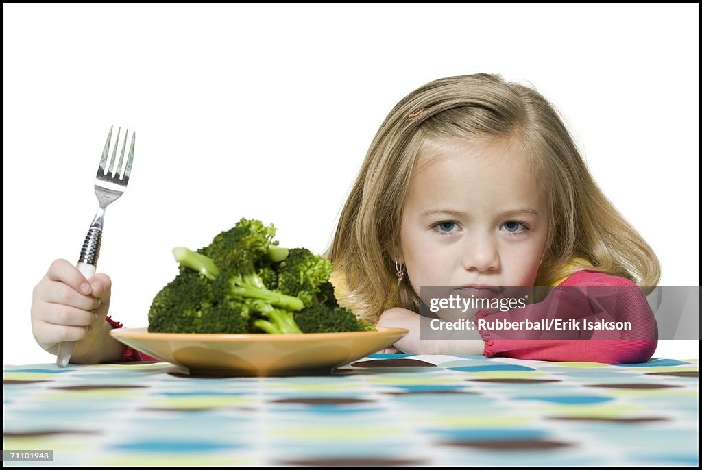Portrait of a girl sitting in front of a plate of broccoli