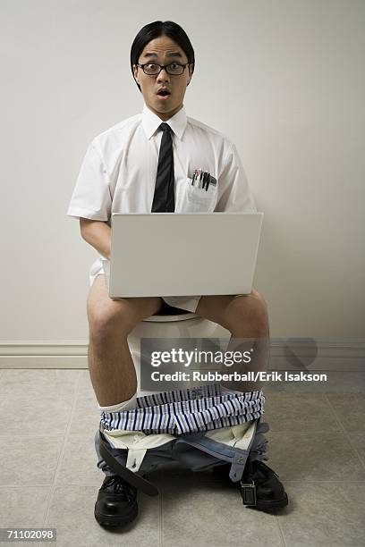 portrait of a young man sitting on a toilet using a laptop - toilet bowl stock pictures, royalty-free photos & images