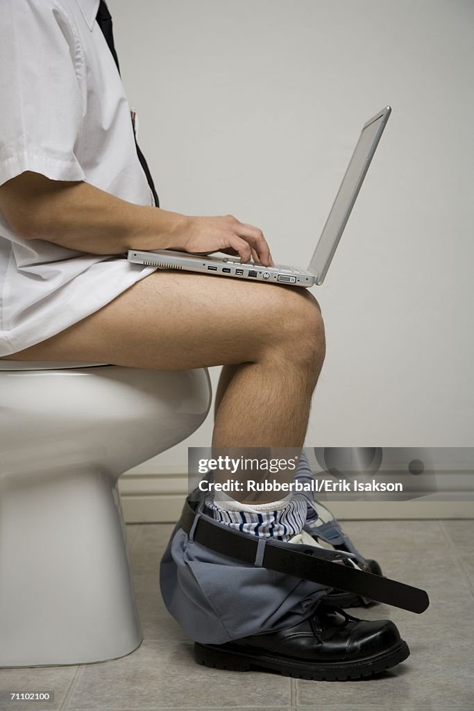 Mid section view of a young man sitting on the toilet seat using a laptop