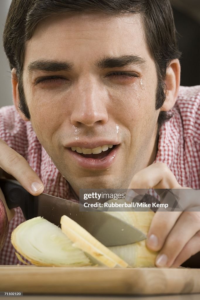 Close-up of a young man with tears in his eyes while cutting onions