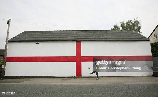 Man plays football next to a giant flag of St George that has been painted on the side of a house on 5 June Lostock Gralam, England. As World Cup...