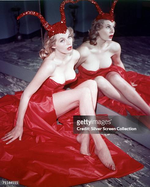 Swedish actress Anita Ekberg sitting by a mirror in a red satin dress and a sequinned devil-horn cap, circa 1956.