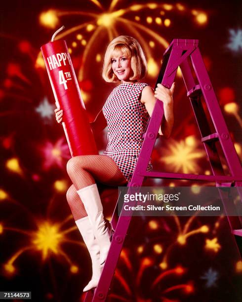 American actress Barbara Eden celebrates the fourth of July up a purple stepladder with a giant firecracker, circa 1965. Eden is best known for her...