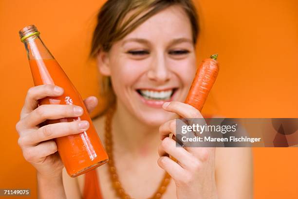 young woman holding carrot and carrot juice, smiling, close-up - carrot juice stock pictures, royalty-free photos & images