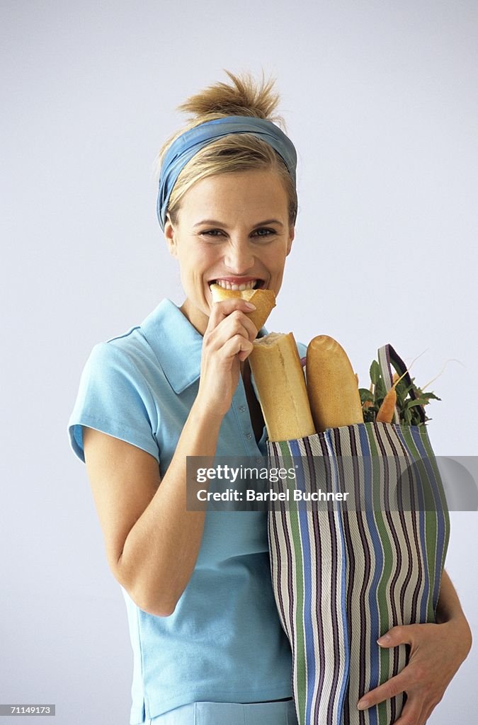 Woman carrying grocery bag, eating baguette