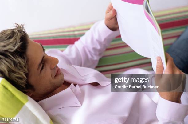 young man lying on sofa, reading book - barbel stock pictures, royalty-free photos & images