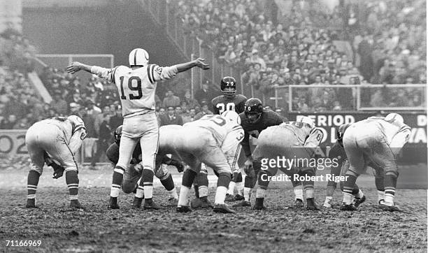 American football player Johnny Unitas, quarterback for the Baltimore Colts, holds his arms out to request quiet from the crowd for the final drive...