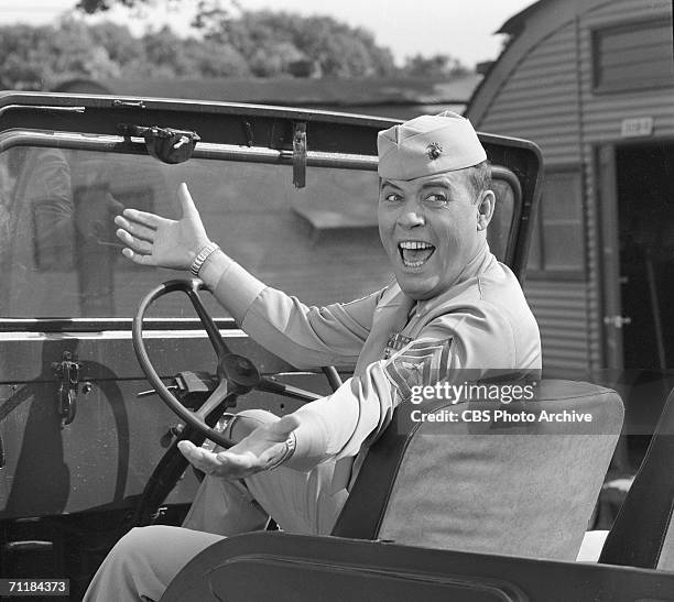 American actor Frank Sutton gestures as he sits in a jeep parked in front of a Quonset hut during an episode of the television comedy series 'Gomer...