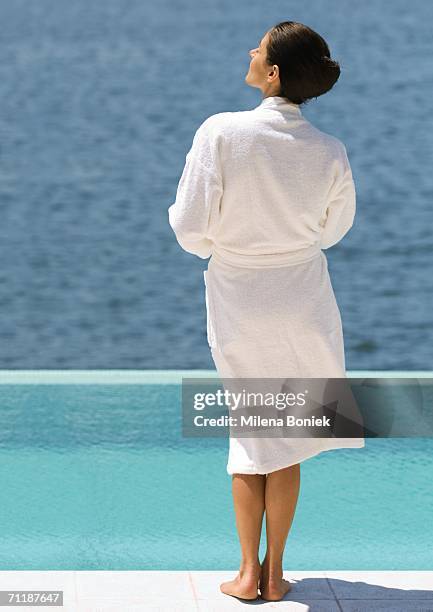 woman in bathrobe standing near pool overlooking sea, rear view - bademantel stock-fotos und bilder