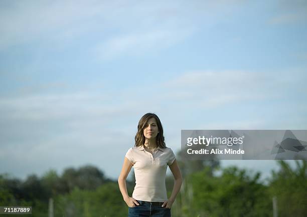 young woman standing with hands in pockets, trees in background - polohemd stock-fotos und bilder