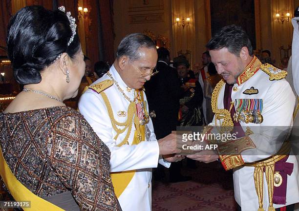 Jordanian King Abdullah II receives a gift from Thailand King Bhumibol Adulyadej while Queen Sirikit looks on at the royal banquet 23 June 2006 in...
