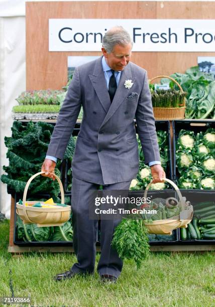 Prince Charles, Prince of Wales pretends to struggle under the weight of two baskets of fresh vegetables given to him as he visits a housing...