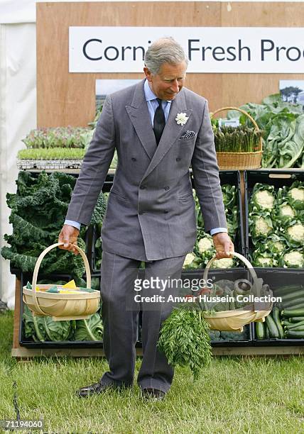 Prince Charles, the Prince of Wales, pretends to struggle under the weight of two baskets of fresh vegetables given to him during a visit to...