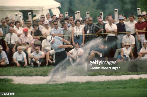 American professional golfer Jack Nicklaus hits the ball from in a sand trap before a crowd of respectful spectators, some of whom watch through...