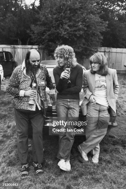 Led Zeppelin manager Peter Grant leans on the hood of a car with the band's singer Robert Plant and bassist John Paul Jones at the Knebworth Music...