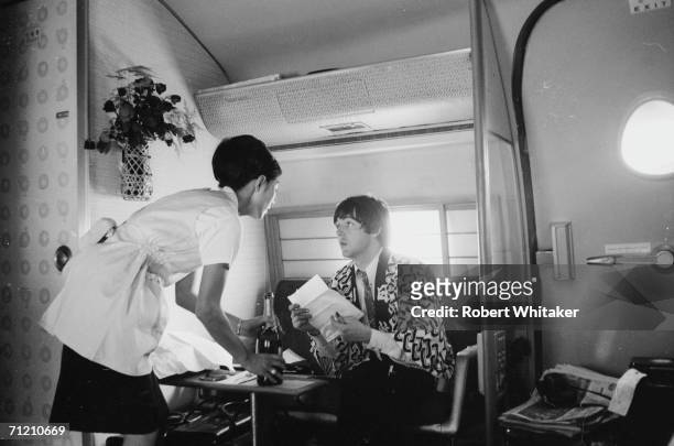 Paul talks to an air stewardess on board a Japan Airlines plane from Anchorage to Tokyo, at the start of the Beatles' Asian tour, 28th June 1966. He...