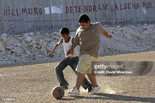 Palestinian boys play a game of soccer, using an old basketball, on a dusty field alongside Israel's separation barrier June 20, 2006 in the West...