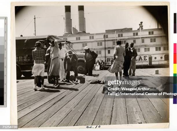 Various concerned men and women, including a policeman, stand by and observe the blanket-covered corpses of three women crushed to death after a...