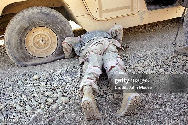 An American soldier checks underneath the chassis of his humvee before fixing a flat tire June 21, 2006 west of Qalat, in the southern province of...