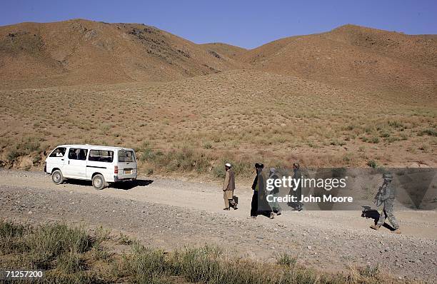 An American soldier walks behind local Afghans after searching their vehicle at an American military checkpoint June 21, 2006 west of Qalat, in the...