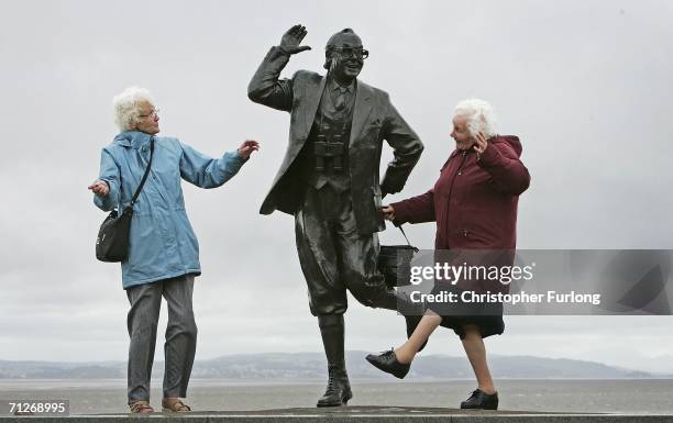 Despite inclement weather pensioners raise a happy smile as they perform the famously British dance of comedians Morcambe and Wise next to a statue...