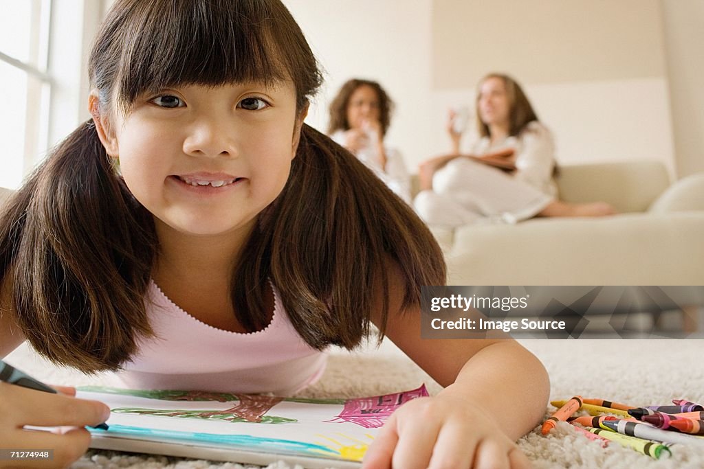 Girl lying in living room with crayons and paper