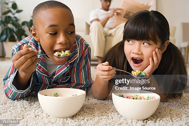 boy and girl lying in living room eating cereal - boy eating cereal stock pictures, royalty-free photos & images