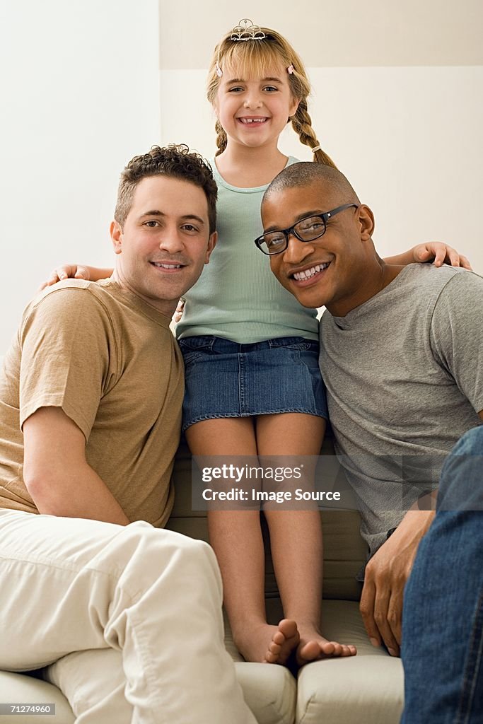 Two men with girl sitting on sofa in living room