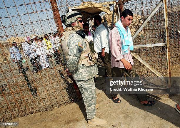 Soldier stands guard as Iraqi freed prisoners walk out of Abu Ghraib prison on June 23, 2006 west of Baghdad, Iraq. More than 500 Iraqi detainees...