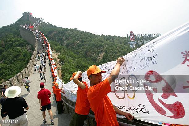 Chinese youths hold flags and an 2008-meter-long Olympics themed scroll as a new landmark which consists of the Beijing 2008 Olympics emblem, the...