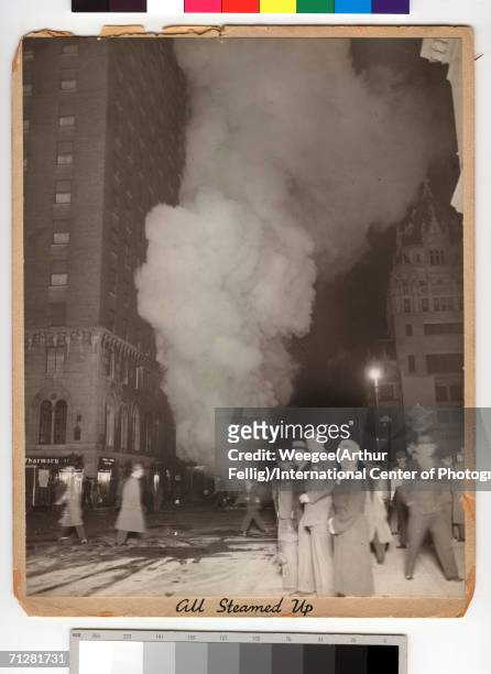 Pedestrians walk up and down Seventh Avenue as a cloud of smoke rises from a fire down the block, New York, New York, early 1940s. Weegee entitled...