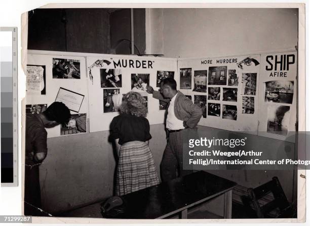 Photography fans examine a series of wall-mounted collages at Weegee's one man exhibition, 'Murder is My Business,' held at the New York Photo...