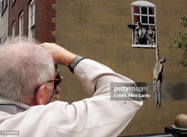 Man takes a photo of a new artwork by the celebrated graffiti artist Banksy on June 27 2006 in Bristol, England. The large graffiti image, depicting...