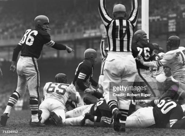 Referee raises his arms to signal a touchdown as American professional football player Otto Graham , quarterback for the Cleveland Browns, kneels in...