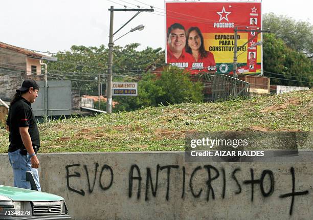 Un hombre observa un graffiti alusivo al presidente boliviano Evo Morales con un cartel de la agrupacion ciudadana Poder Democratico y Social al...