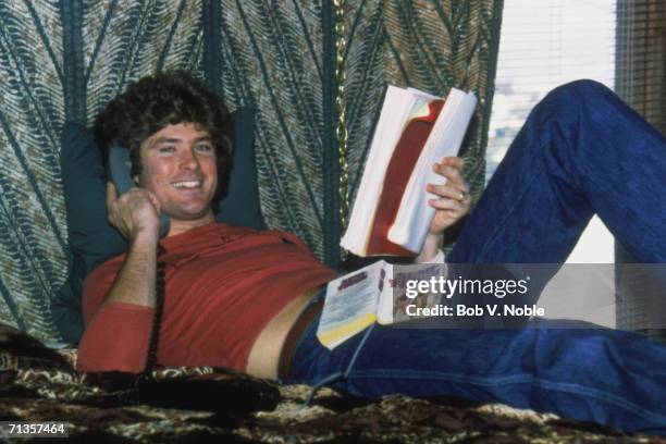 Actor and singer David Hasselhoff, at home in Hollywood, reading a script and an American football novel 'Semi Tough' while making a phone call, 1979.