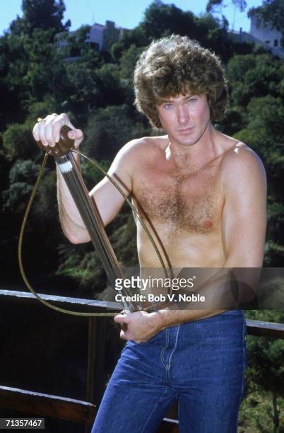 American actor and singer David Hasselhoff at home in Hollywood, stripped to the waist posing with a bullworker, 1979.