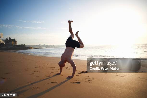 mature man doing handstand on sunlit beach, cascais, portugal - handstand beach stock pictures, royalty-free photos & images