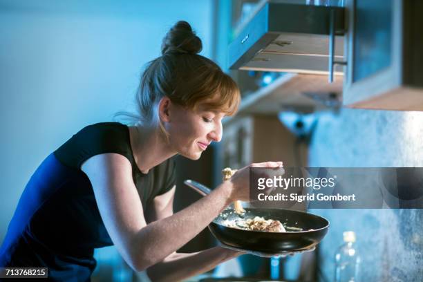 young woman tasting food from frying pan - sigrid gombert stock-fotos und bilder