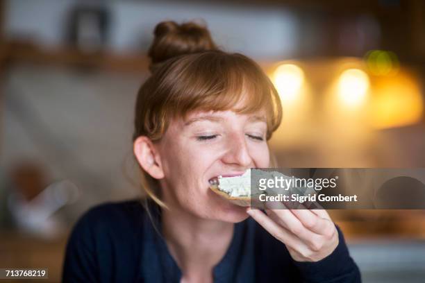 young woman eating bread with cream cheese - indulgence stockfoto's en -beelden