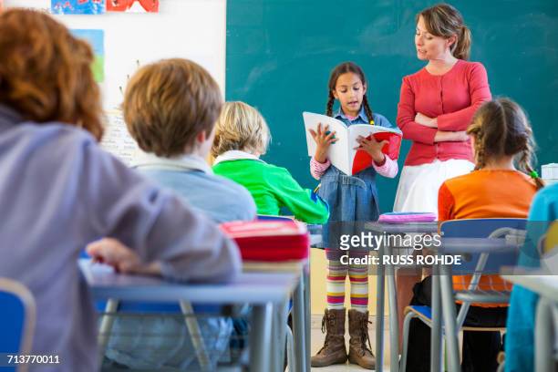 primary schoolgirl reading at front of classroom - teacher in front of class stock pictures, royalty-free photos & images